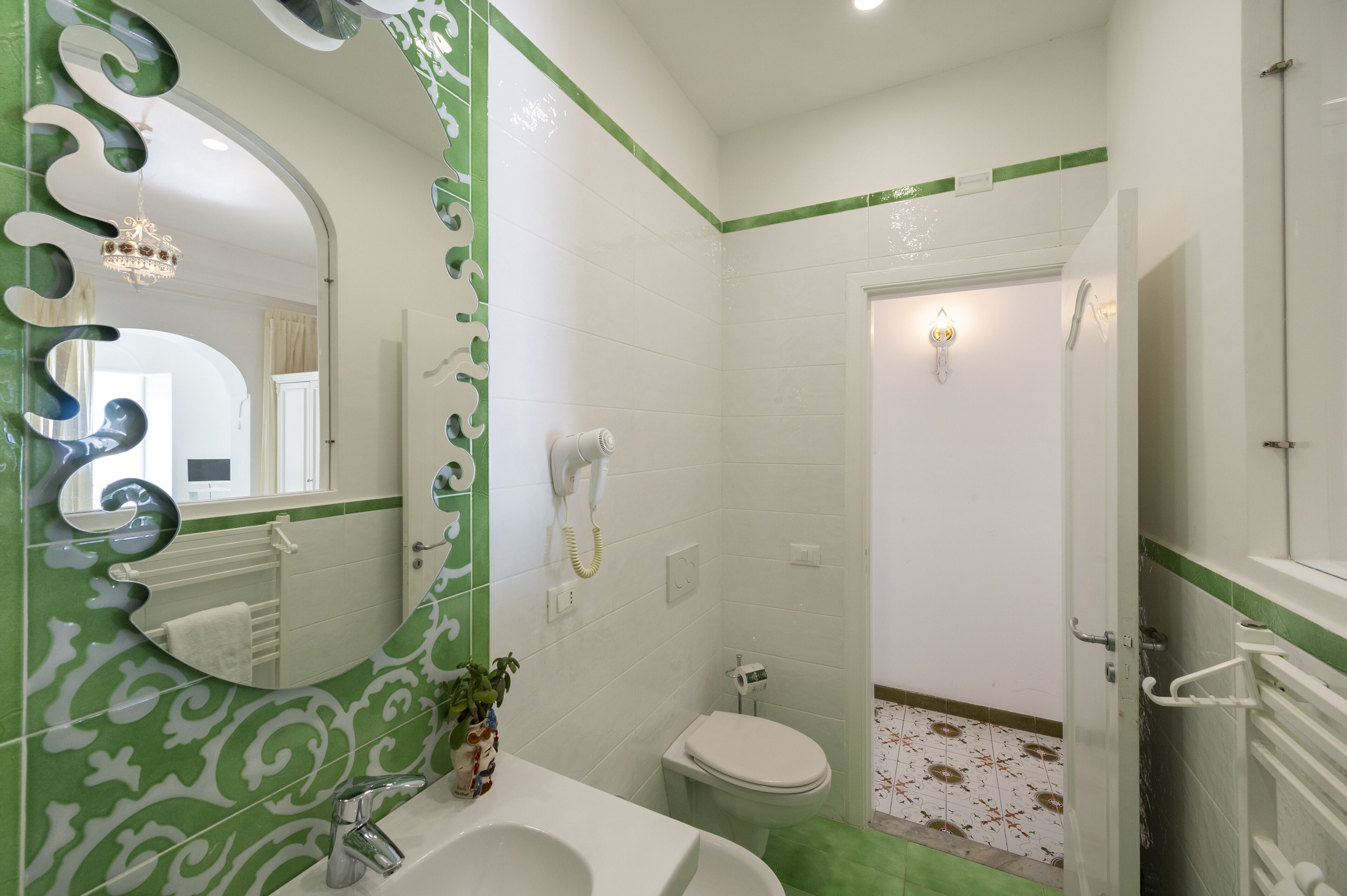 A bathroom with a white sink, a toilet, a shower, and a mirror with a green and white pattern.