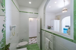 A bathroom with a white toilet, a hairdryer, a towel rack, and a shower area. - Il Barilotto (Positano)