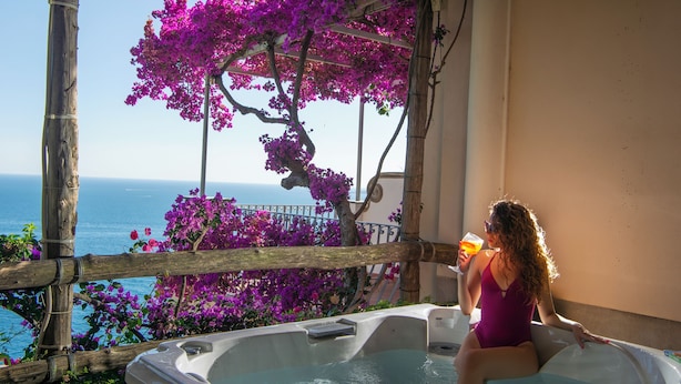 A woman in a purple swimsuit sitting in a hot tub with a view of the sea and purple flowers. - Il Barilotto (Positano)