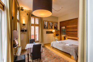 Habitación de hotel con cama, escritorio, silla, mesa, televisión y ventana con cortinas.