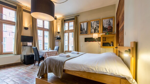Une chambre d’hôtel avec un lit en bois, un bureau avec une chaise, une table et une fenêtre avec des rideaux.