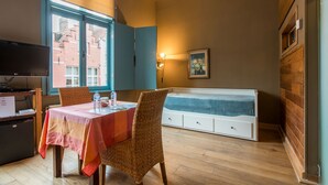 Une pièce comprenant une table à manger, des chaises, un banc, un téléviseur et une fenêtre donnant sur des immeubles.