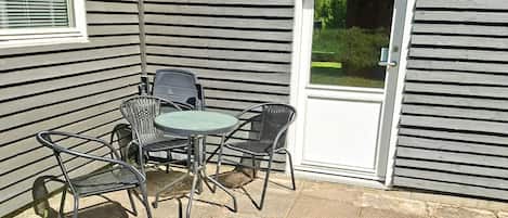 A patio with a table and four chairs, a door, and a window with blinds.