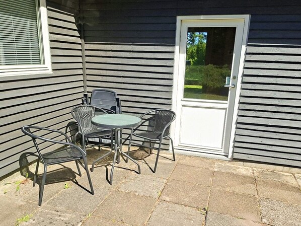 A patio with a table and four chairs, a door, and a window with blinds.