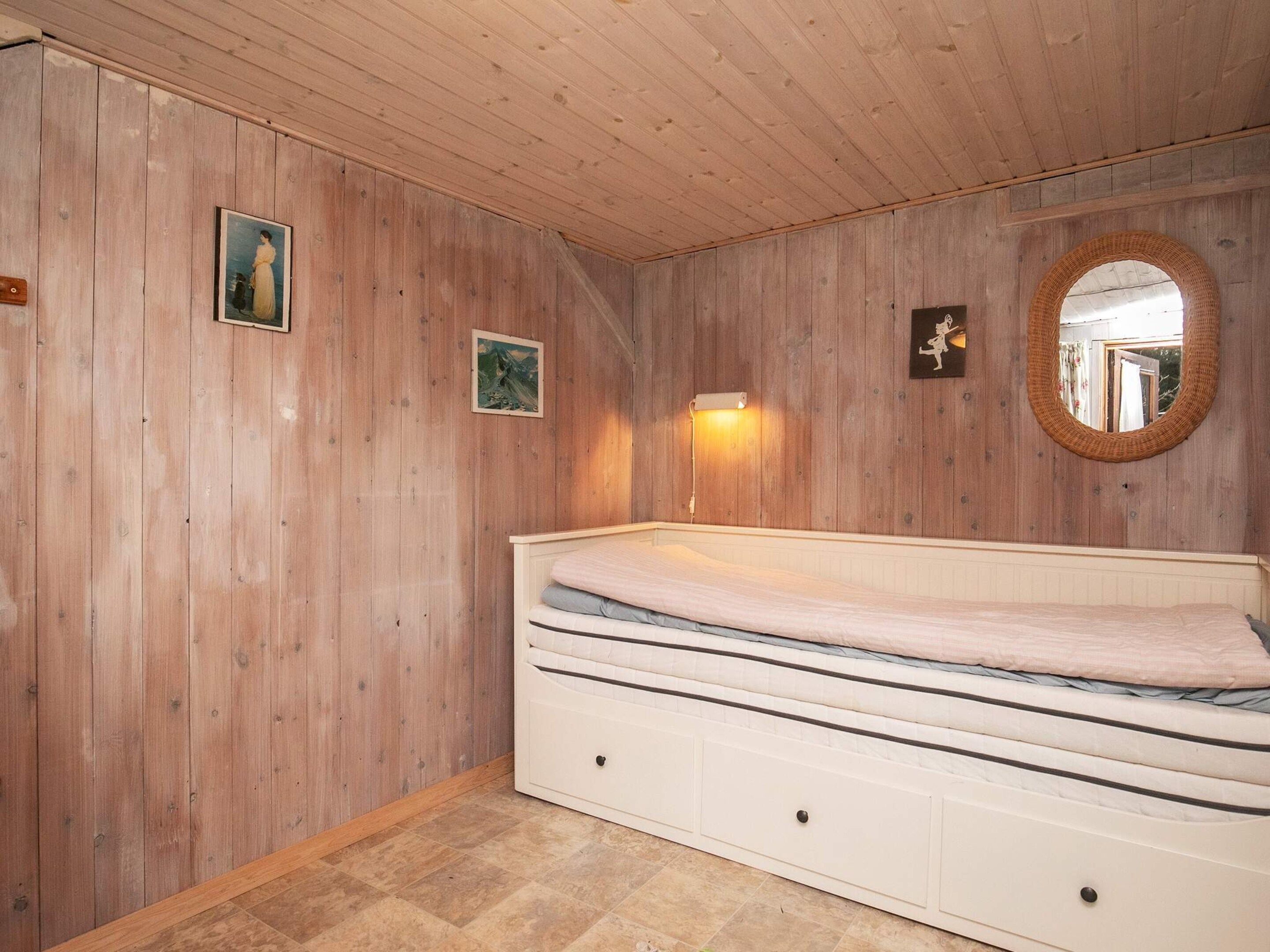 Une chambre avec des murs en bois, un lit, une lampe fixée au mur et un miroir.
