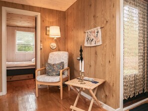 A cozy room with a wooden floor, a bed with white bedding, a patterned armchair with a cushion, a small table with a lamp, and a wall hanging. - 5 Person Holiday Home in Fjerritslev (Fjerritslev)
