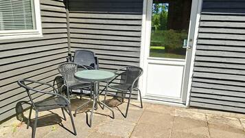 Un patio con una mesa y cuatro sillas, una puerta y una ventana con persianas.