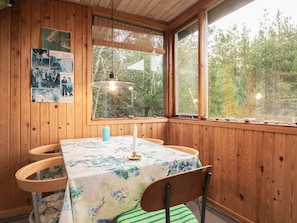 A wooden-paneled room with a table set for two, a hanging light fixture, and a window with a view of trees.