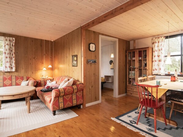 Una habitación acogedora con techo de madera, un sofá, una mesa de comedor con sillas y una estantería.