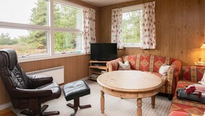 A cozy living room with a leather chair, a sofa, a round wooden table, and a television.