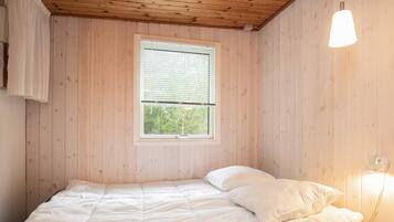 A single bed with white bedding in a room with wooden walls and a window with blinds.
