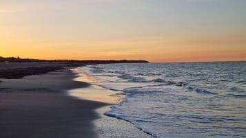 Una playa con un mar tranquilo, una orilla arenosa y una masa de tierra a lo lejos.