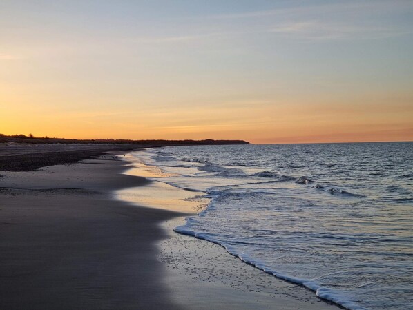 A beach with a calm sea, a sandy shore, and a distant landmass.