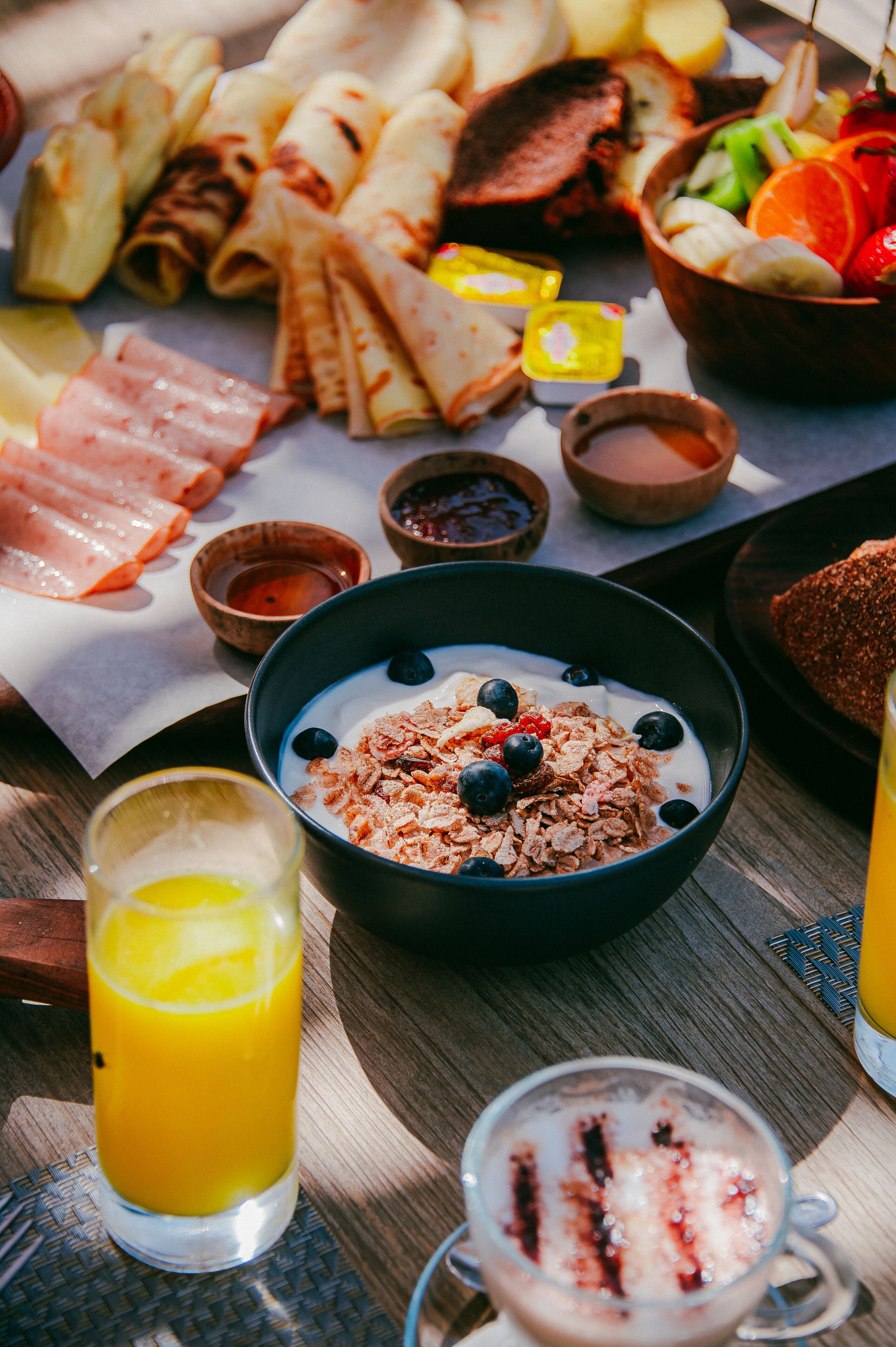 A breakfast table with various food items, including a bowl of cereal with blueberries, a glass of orange juice, and a hot beverage with whipped cream.