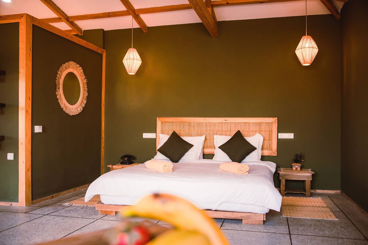 Un dormitorio con cabecera de madera, dos mesitas de noche, un espejo y dos lámparas colgantes.