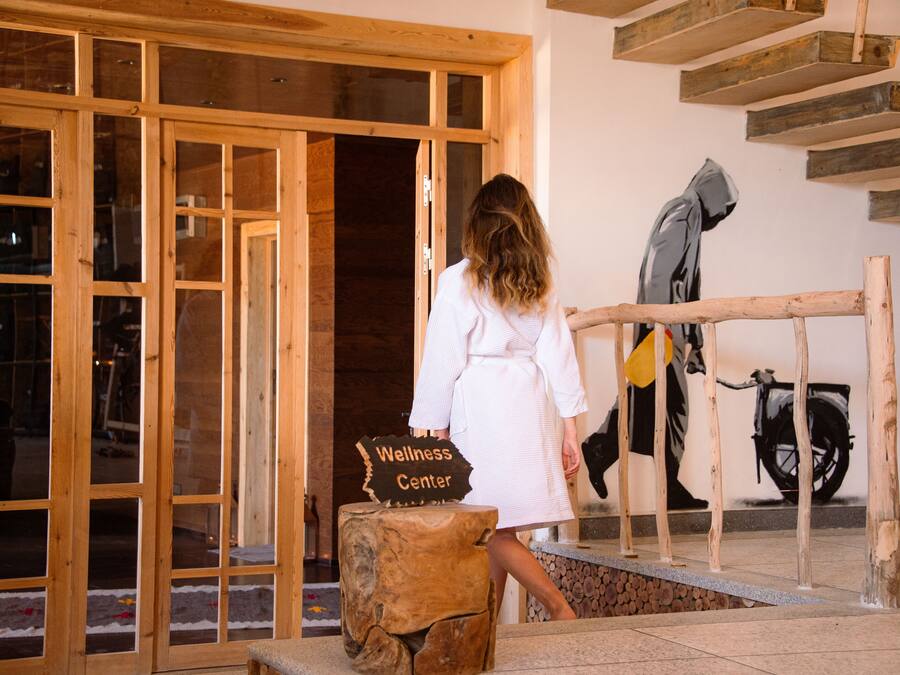 Une entrée avec un cadre en bois, sur laquelle est apposée une enseigne indiquant « Centre de bien-être », et une personne vêtue d’une robe blanche, debout à côté d’un tabouret en bois.
