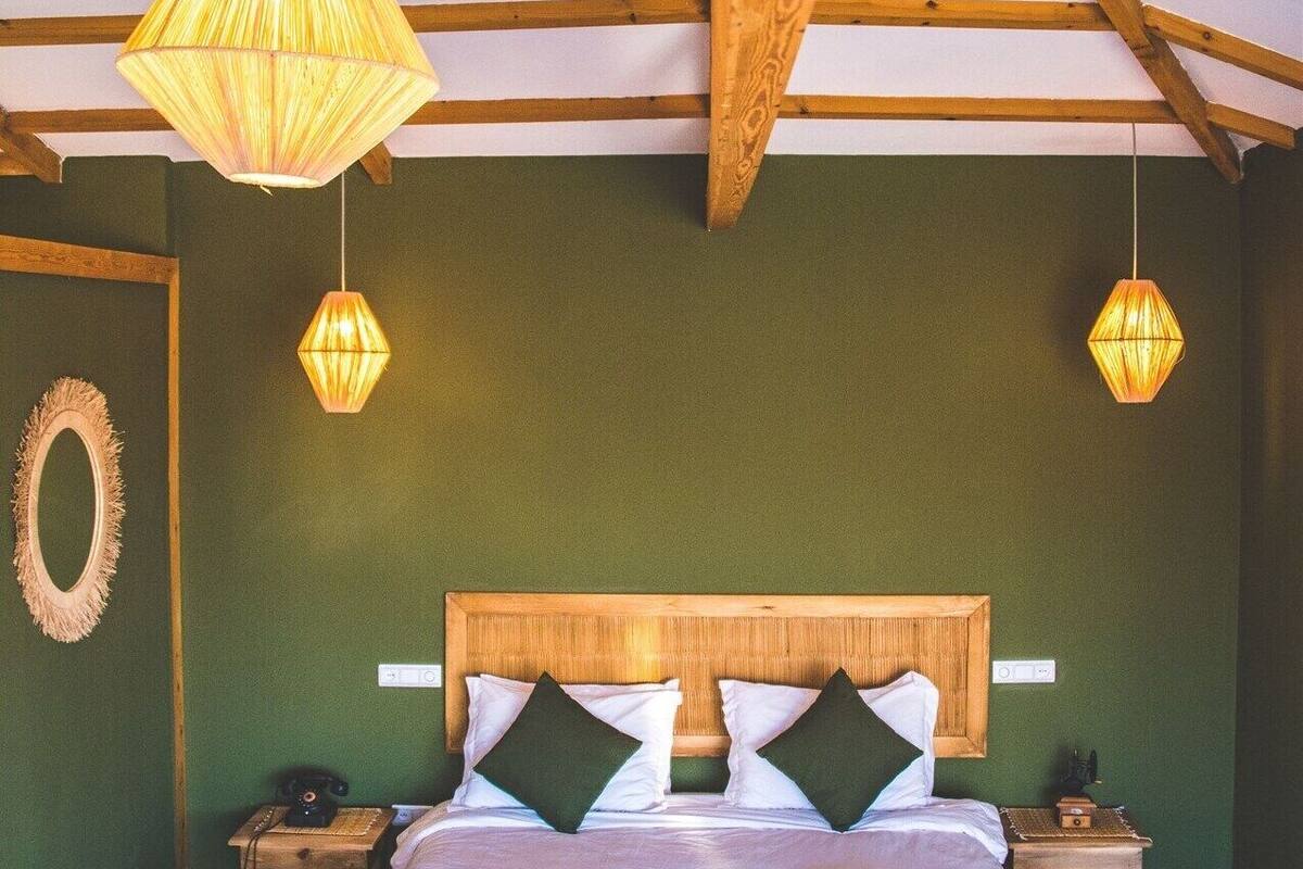 Un dormitorio con techo de madera, una cama con ropa de cama blanca, dos mesitas de noche y dos lámparas colgantes.