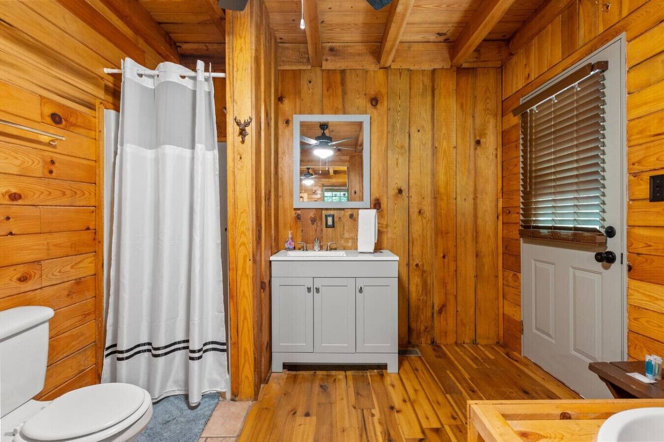 A wooden cabin bathroom with a toilet, sink, and shower curtain.
