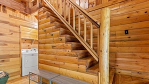 A wooden staircase in a cabin with a washing machine and a bench at the bottom. - The Road`s End- Pet Friendly, Hot Tub, Firepit, Covered Deck (Pine Ridge)