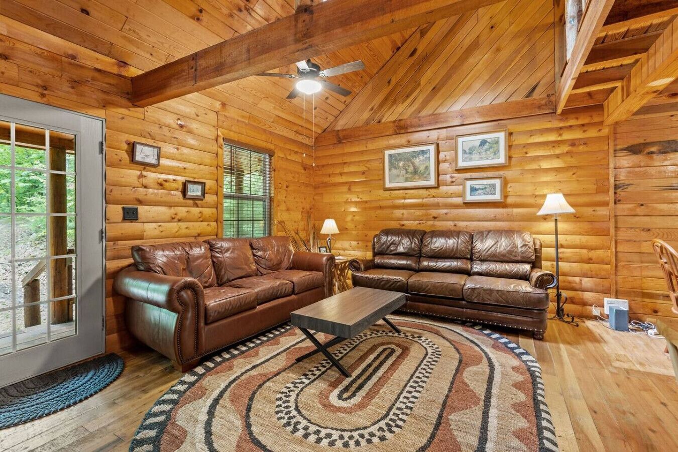 Ein Interieur einer Blockhütte mit zwei Ledersofas, einem Couchtisch und einem gemusterten Teppich.