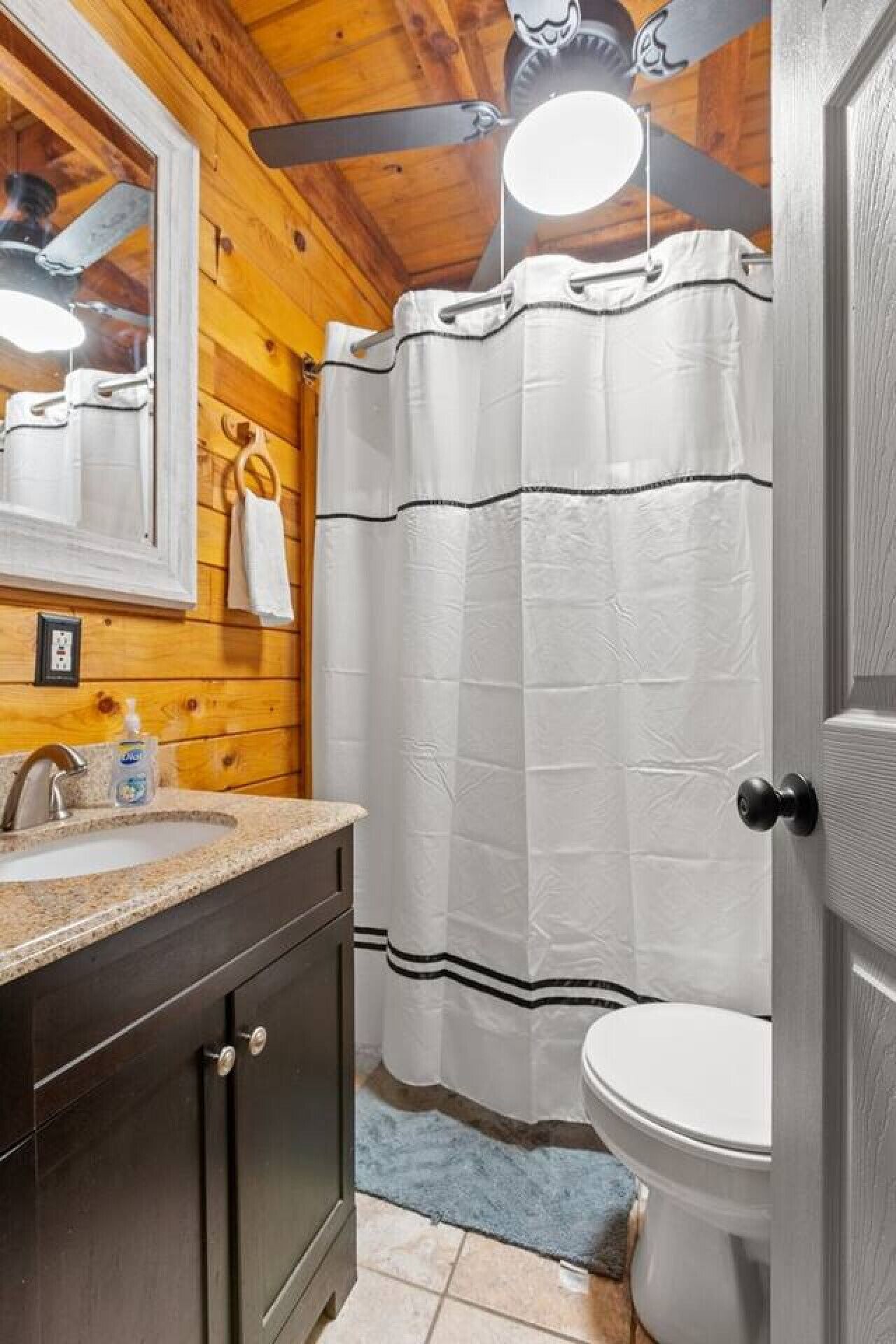 Un baño con techo de madera, un lavamanos con dispensador de jabón, un inodoro y una cortina de ducha.