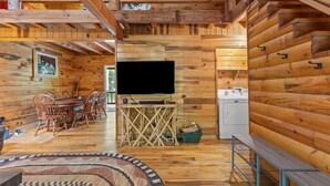 A wooden cabin interior with a dining area, a TV, and a washing machine. - The Road`s End- Pet Friendly, Hot Tub, Firepit, Covered Deck (Pine Ridge)