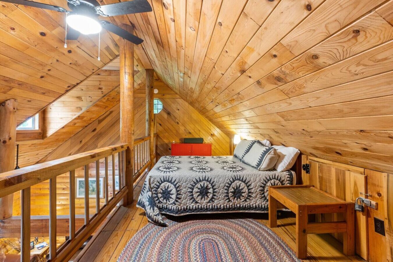A cozy attic bedroom with a wooden ceiling, a bed with patterned bedding, a small table, and a window.