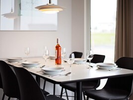 A dining table set with plates, glasses, and a bottle, surrounded by chairs.