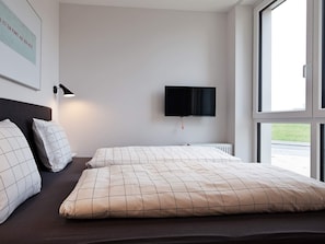 A hotel room with a bed, a flat-screen TV mounted on the wall, and a window providing a view of the outside. - 5 Star Holiday Home in Wendtorf (Wendtorf)