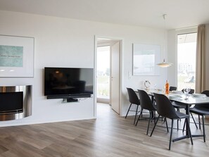 A modern living room with a flat-screen TV, a fireplace, and a dining area with chairs and a table.