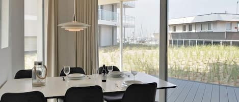A modern dining area with a large table, black chairs, and a view of a marina through large windows.