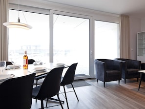 A modern dining area with a table set for two, a bottle of wine, and a view through large glass doors. - 5 Star Holiday Home in Wendtorf (Wendtorf)