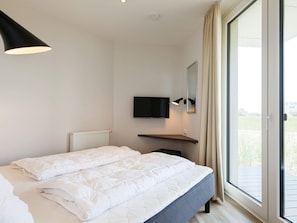 Un dormitorio moderno con cama, televisor y puerta corrediza al exterior.