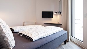 A modern bedroom with a bed, a mounted TV, a bedside table, and a window with curtains. - 5 Star Holiday Home in Wendtorf (Wendtorf)