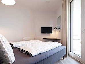 Quarto moderno com cama, televisão na parede, mesa de cabeceira e janela com cortinas.