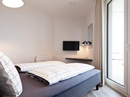 A modern bedroom with a bed, a mounted TV, a bedside table, and a window with curtains.
