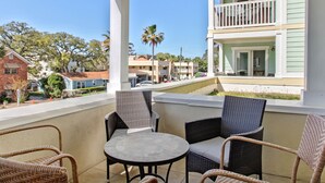A balcony with wicker chairs and a table, overlooking a residential area with houses and palm trees. - Rooftop Pool Access, Walk to Beach and Tybrisa (Tybee Island)