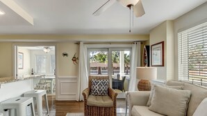 A spacious living room with a beige sofa, a wicker chair, and a ceiling fan. - Rooftop Pool Access, Walk to Beach and Tybrisa (Tybee Island)