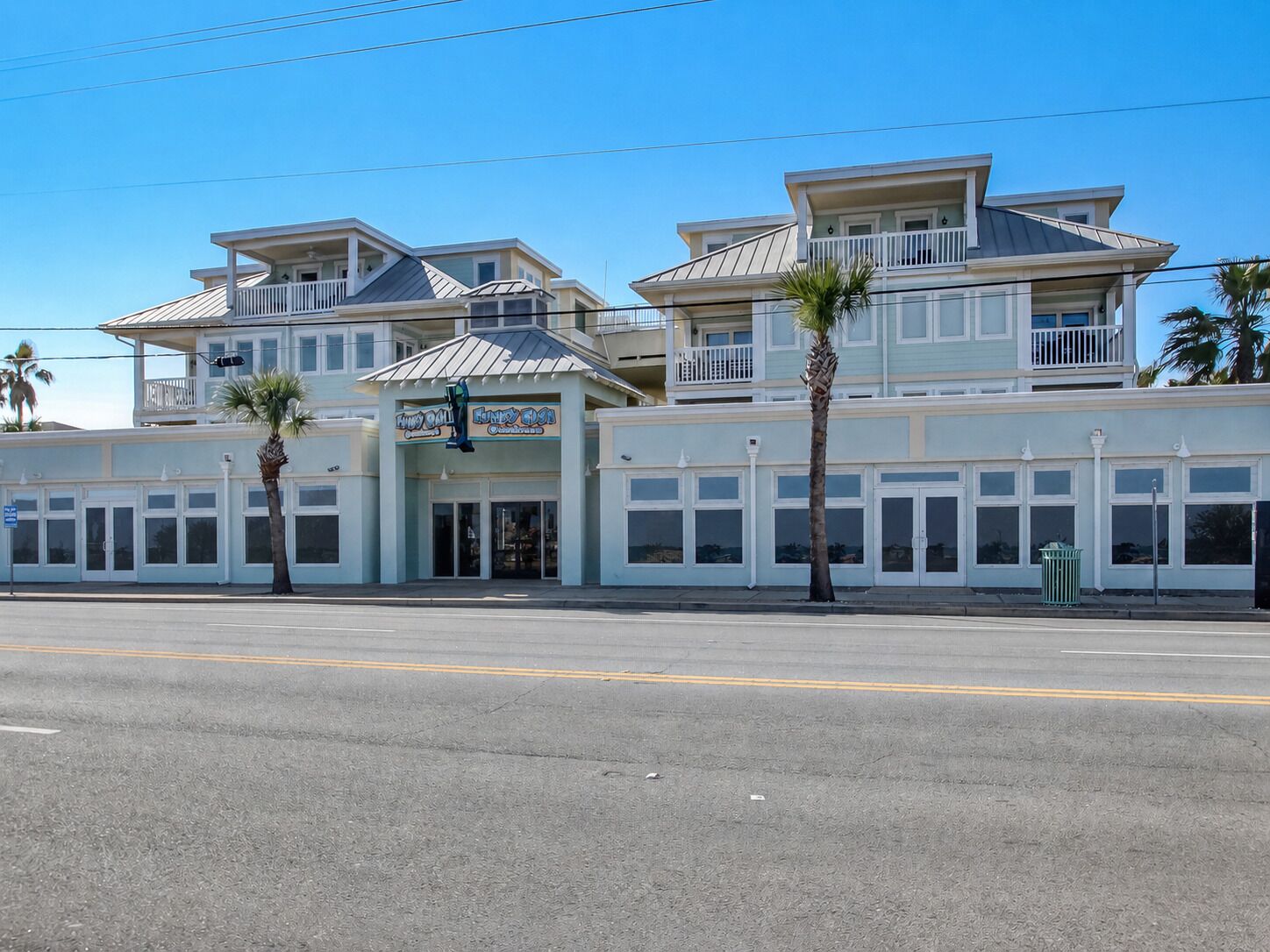 A multi-story building with a balcony, storefronts, and palm trees.
