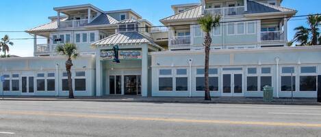 A multi-story building with a balcony, storefronts, and palm trees.