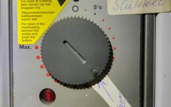 A close-up of a mechanical part with a label, a red button, and a temperature indicator.