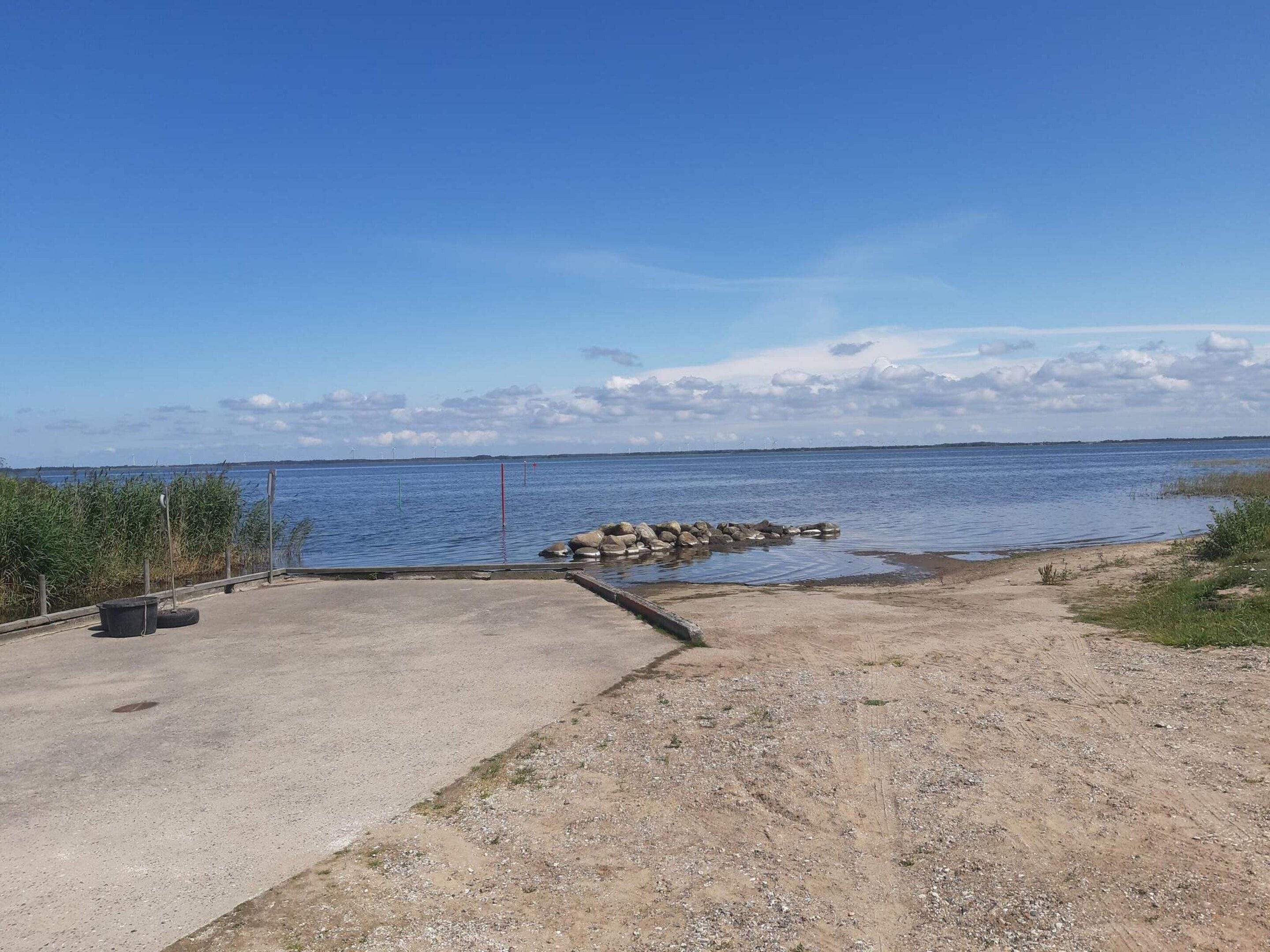 Una zona costiera con un sentiero in cemento che conduce a una costa rocciosa, cielo sereno e mare calmo.