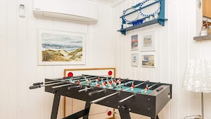 Uma mesa de futebol de mesa em um quarto com paredes brancas, um quadro emoldurado e uma estante azul com objetos decorativos.