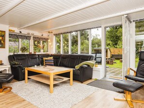 A modern living room with a leather sofa, a wooden coffee table, and a large window offering a view of the garden. - 6 Person Holiday Home in Ulfborg (Ulfborg)
