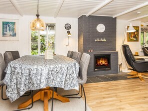 A modern living room with a fireplace, a round table with chairs, and a large window with a view of greenery. - 6 Person Holiday Home in Ulfborg (Ulfborg)