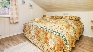 Quarto com teto inclinado, piso de madeira, colcha estampada e janela com cortinas.
