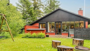 Ein modernes Haus mit roter Fassade, einer Holzschaukel und einem Rasen mit Holzstümpfen.