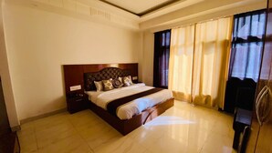 Habitación de hotel con una cama grande, una mesita de noche, un armario y una ventana con cortinas.