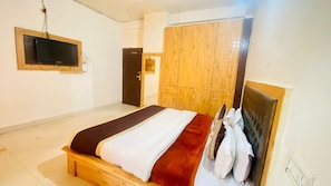 Un dormitorio con cama, armario, televisor montado en la pared y una puerta.