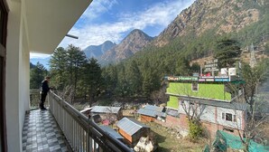 Un balcón con vista a un paisaje montañoso, una persona de pie y un edificio con el letrero 'Delhi Heights'.
